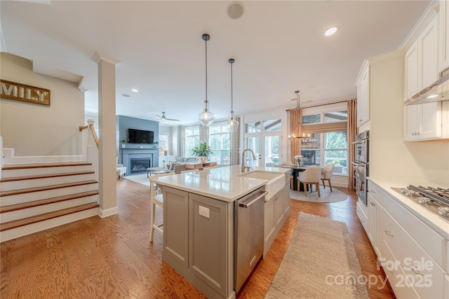5256 Meadowcroft Way, Fort Mill, SC 29708 - kitchen featuring appliances with stainless steel finishes, a fireplace, light wood-style flooring, a kitchen island with sink, and a kitchen bar