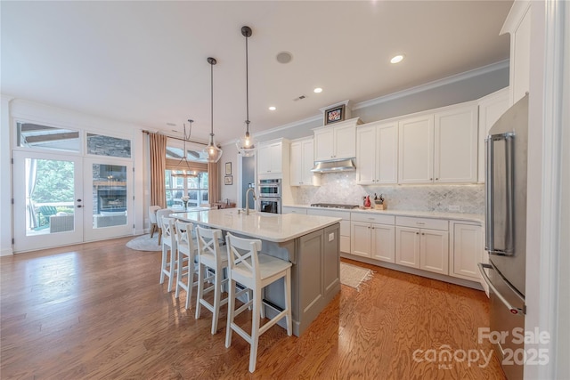 5256 Meadowcroft Way, Fort Mill, SC 29708 - kitchen featuring appliances with stainless steel finishes, under cabinet range hood, ornamental molding, white cabinets, and tasteful backsplash