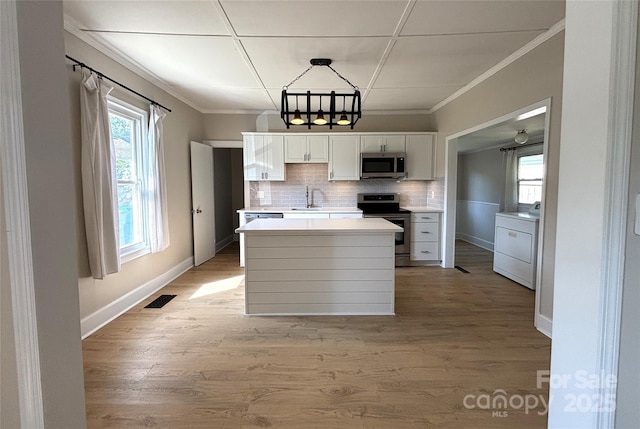 339 Mayflower Ave, Cramerton, NC 28032 - kitchen with appliances with stainless steel finishes, washer / dryer, white cabinets, crown molding, and a chandelier