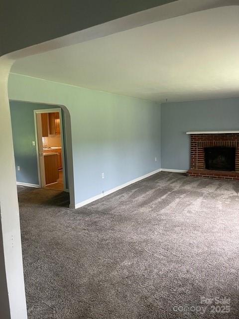 unfurnished living room with carpet floors, a fireplace, and arched walkways
