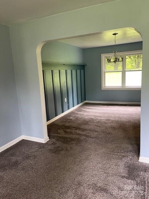 spare room featuring arched walkways, carpet flooring, and a chandelier