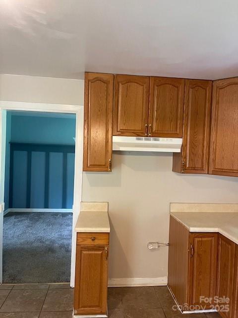 kitchen with under cabinet range hood, brown cabinetry, and dark tile patterned floors