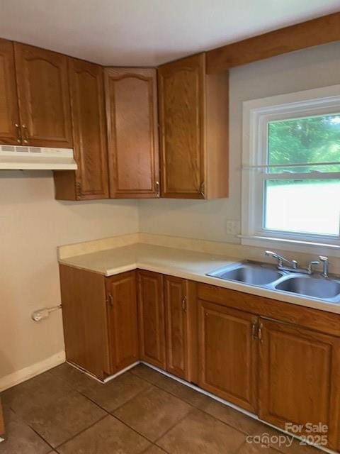 kitchen with under cabinet range hood, brown cabinets, dark tile patterned floors, and light countertops
