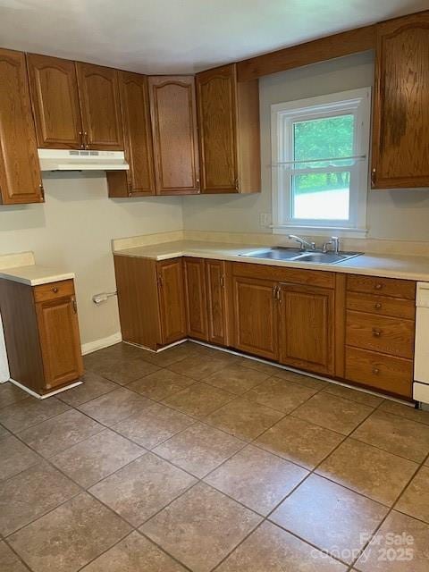 kitchen featuring under cabinet range hood, brown cabinets, light countertops, and tile patterned floors
