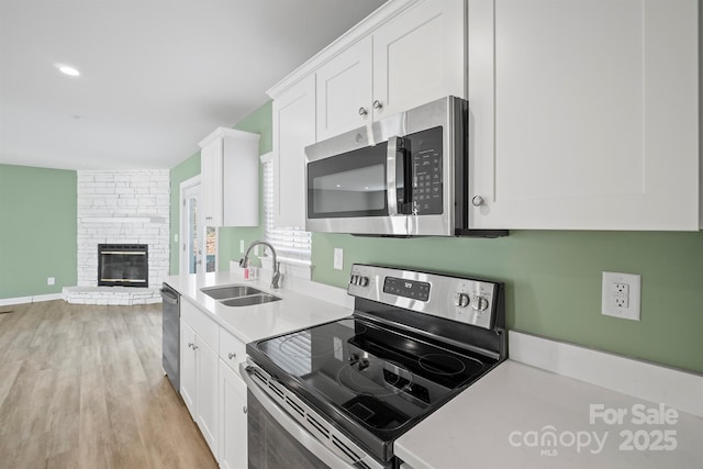 3433 Spinner Ct, Sherrills Ford, NC 28673 - kitchen featuring stainless steel appliances, light countertops, white cabinets, light wood-type flooring, and a large fireplace