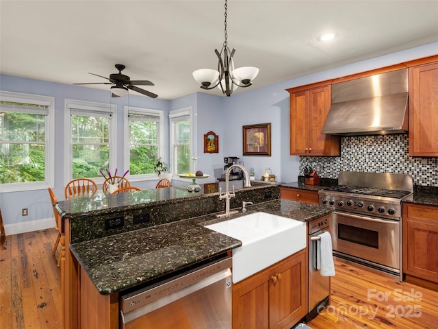303 S Braeside Ct, Asheville, NC 28803 - kitchen featuring appliances with stainless steel finishes, wall chimney exhaust hood, brown cabinets, light wood-style flooring, and recessed lighting