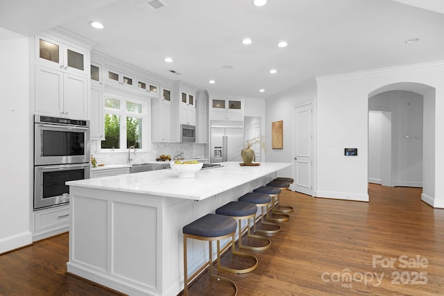 7912 Baltusrol Ln, Charlotte, NC 28210 - kitchen featuring built in appliances, a center island, arched walkways, white cabinetry, and recessed lighting