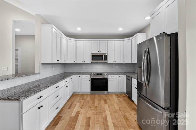 1019 Null Rd, Lincolnton, NC 28092 - kitchen with appliances with stainless steel finishes, white cabinetry, dark stone countertops, light wood-style flooring, and backsplash
