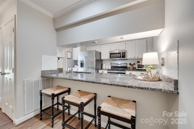 353 Tall Oaks Trl, Fort Mill, SC 29715 - kitchen featuring appliances with stainless steel finishes, a peninsula, light wood-style flooring, ornamental molding, and stone countertops