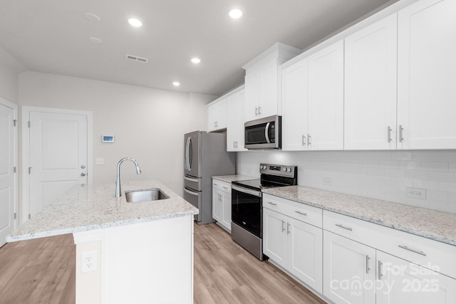 1022 Jeffery Dean Ct, Albemarle, NC 28001 - kitchen featuring stainless steel appliances, an island with sink, light wood-style floors, tasteful backsplash, and white cabinets