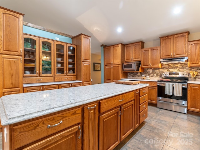 21 Fern Haven Ln, Fairview, NC 28730 - kitchen featuring appliances with stainless steel finishes, under cabinet range hood, tasteful backsplash, brown cabinets, and glass insert cabinets