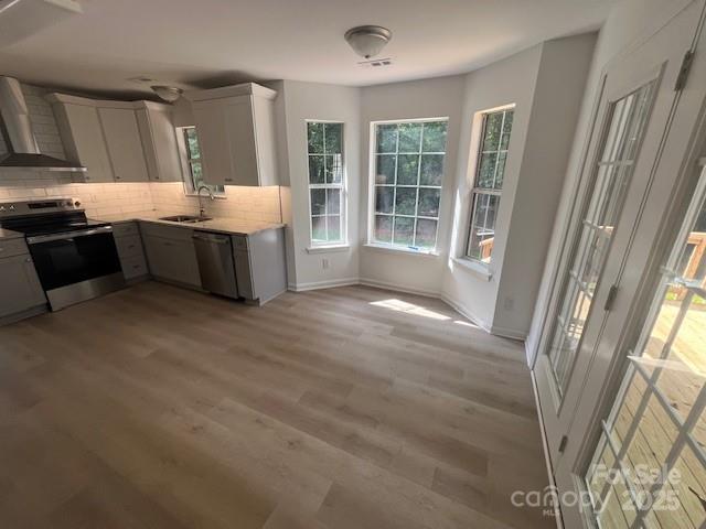 11021 Scrimshaw Ln, Charlotte, NC 28215 - kitchen with stainless steel appliances, wall chimney range hood, light countertops, decorative backsplash, and light wood-type flooring