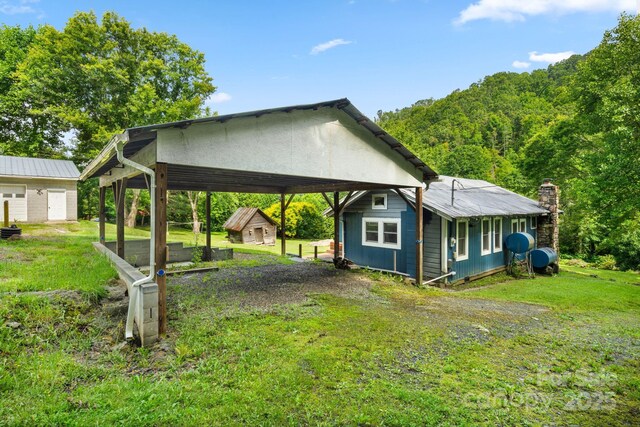 2428 Hamburg Rd, Mars Hill, NC 28754 - view of side of property featuring a storage unit, driveway, a detached carport, a yard, and a view of trees