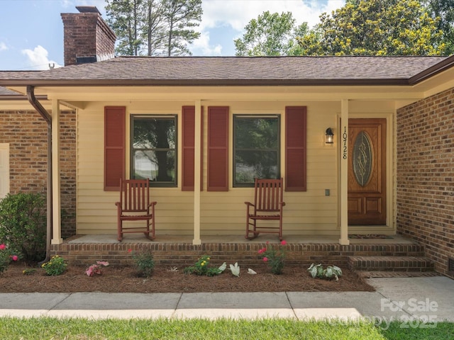 10728 Forest Dr, Matthews, NC 28105 - property entrance featuring covered porch, a chimney, brick siding, and a shingled roof