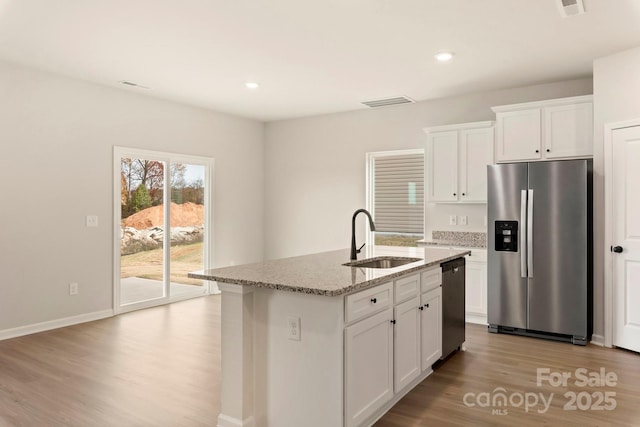 1059 Russell Dr, Winston Salem, NC 27127 - kitchen featuring appliances with stainless steel finishes, wood finished floors, light stone countertops, white cabinetry, and a kitchen island with sink