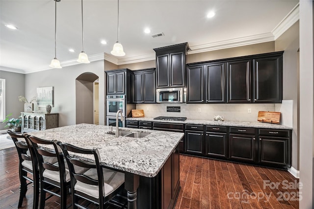 16547 Bastille Dr, Charlotte, NC 28278 - kitchen with appliances with stainless steel finishes, arched walkways, dark cabinets, an island with sink, and light stone countertops