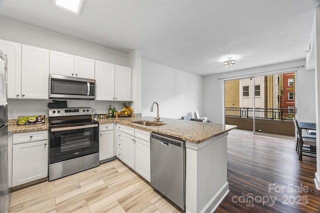 1315 E Blvd Unit 321, Charlotte, NC 28203 - kitchen with stainless steel appliances, a peninsula, white cabinets, light wood-type flooring, and light stone counters