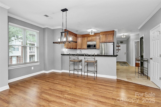 921 NE Dr, Davidson, NC 28036 - kitchen featuring stainless steel appliances, light wood-type flooring, crown molding, dark countertops, and brown cabinetry