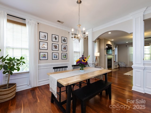 12928 Windy Lea Ln, Huntersville, NC 28078 - dining room featuring arched walkways, a glass covered fireplace, dark wood-style flooring, decorative columns, and a wainscoted wall