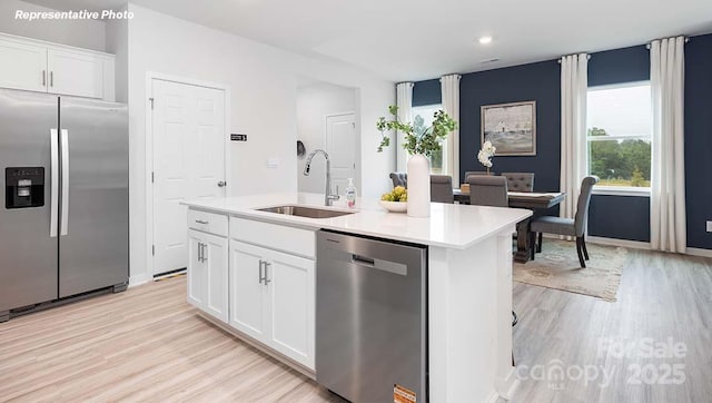 12020 Zazu Way, Charlotte, NC 28215 - kitchen featuring appliances with stainless steel finishes, light wood-style flooring, white cabinets, an island with sink, and light countertops