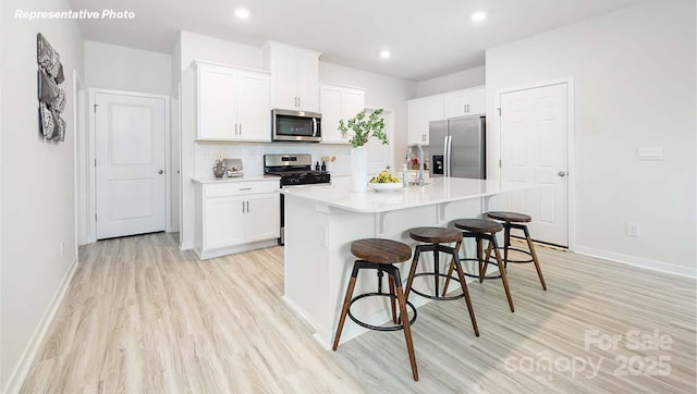 12020 Zazu Way, Charlotte, NC 28215 - kitchen with appliances with stainless steel finishes, light wood-type flooring, a breakfast bar, white cabinetry, and a kitchen island with sink