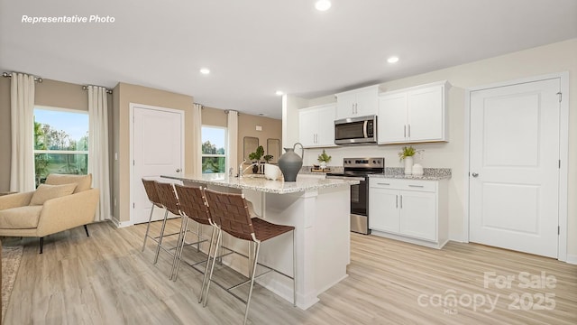 12019 Zazu Way, Charlotte, NC 28215 - kitchen with appliances with stainless steel finishes, light wood-style flooring, a kitchen bar, a center island with sink, and light stone counters
