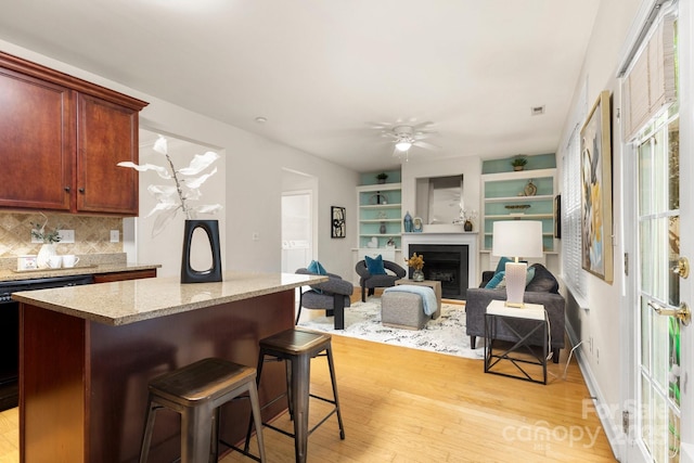 4442 Coventry Row Ct, Charlotte, NC 28270 - kitchen featuring light wood-style floors, decorative backsplash, a kitchen bar, a center island, and a fireplace