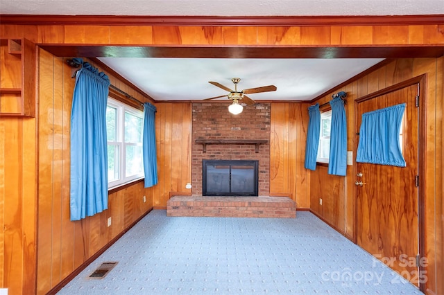 1216 Manchester Ln, Charlotte, NC 28227 - unfurnished living room featuring a ceiling fan, wood walls, a brick fireplace, crown molding, and carpet floors