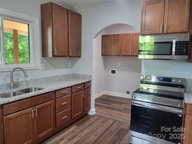 94 James St SW, Concord, NC 28025 - kitchen featuring stainless steel appliances, dark wood finished floors, light stone countertops, arched walkways, and brown cabinets