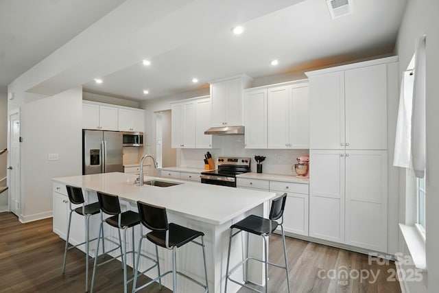 812 Dogwood Creek Ln, Indian Trail, NC 28079 - kitchen with appliances with stainless steel finishes, under cabinet range hood, wood finished floors, a breakfast bar area, and white cabinetry