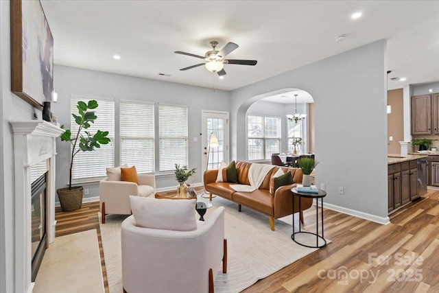 2527 Fossil Stone Ln, Fort Mill, SC 29708 - living area featuring arched walkways, a chandelier, light wood-style flooring, a ceiling fan, and a glass covered fireplace