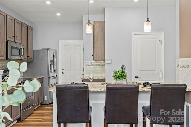 2527 Fossil Stone Ln, Fort Mill, SC 29708 - kitchen featuring appliances with stainless steel finishes, backsplash, light wood-type flooring, light stone counters, and hanging light fixtures