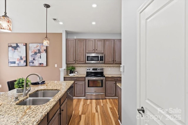 2527 Fossil Stone Ln, Fort Mill, SC 29708 - kitchen with stainless steel appliances, light wood-type flooring, backsplash, decorative light fixtures, and light stone counters
