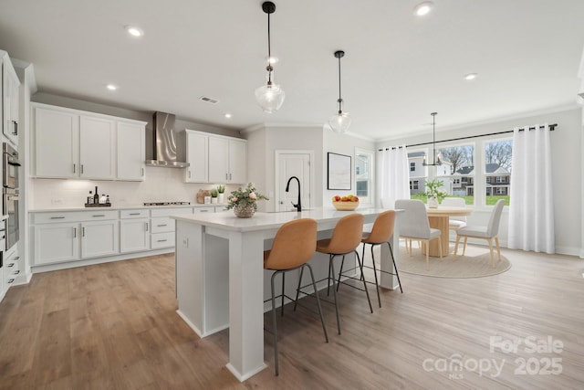 204 Coronado Ave, Matthews, NC 28104 - kitchen featuring wall chimney range hood, crown molding, stovetop, light countertops, and light wood-style floors