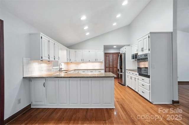4323 Crow Rd, Monroe, NC 28112 - kitchen with stainless steel appliances, a peninsula, vaulted ceiling, light stone counters, and light wood-style flooring