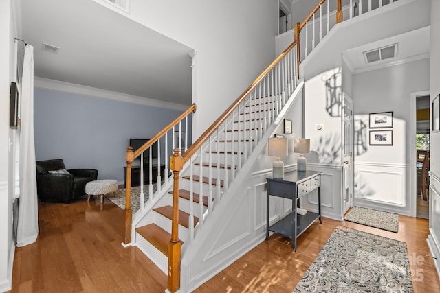 13934 Kings Carriage Ln, Charlotte, NC 28278 - stairway with crown molding, wood finished floors, a towering ceiling, and a wainscoted wall