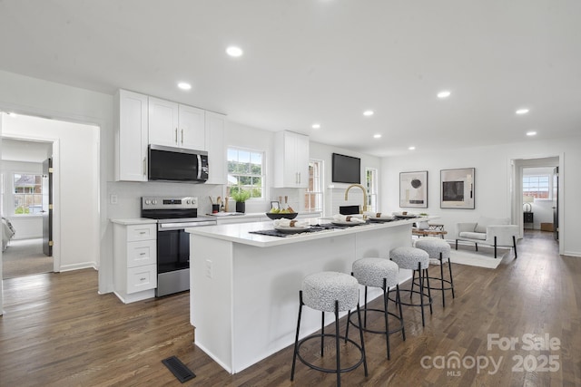 5817 Red Carriage Ln, Charlotte, NC 28212 - kitchen featuring stainless steel appliances, an island with sink, white cabinets, a kitchen breakfast bar, and dark wood-style flooring