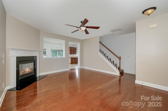 124 Glade Valley Ave, Mooresville, NC 28117 - unfurnished living room with wood finished floors, a ceiling fan, stairs, and a glass covered fireplace