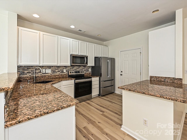 12131 Honor Guard Ave, Charlotte, NC 28277 - kitchen featuring appliances with stainless steel finishes, a peninsula, light wood-style floors, dark stone countertops, and white cabinets