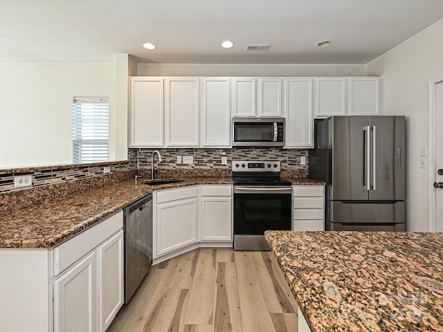 12131 Honor Guard Ave, Charlotte, NC 28277 - kitchen featuring appliances with stainless steel finishes, dark stone counters, light wood finished floors, white cabinets, and tasteful backsplash