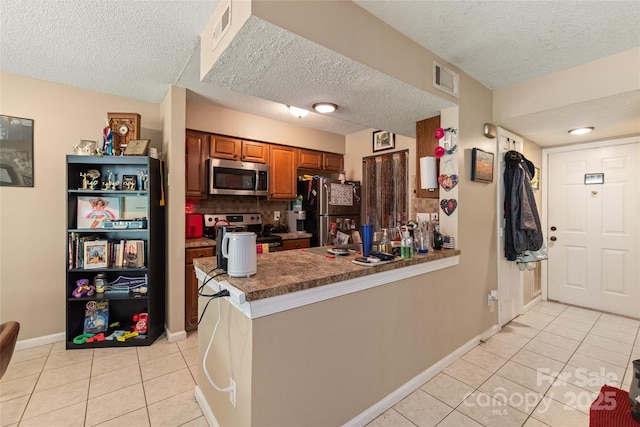 11069 Running Ridge Rd, Charlotte, NC 28226 - kitchen with appliances with stainless steel finishes, brown cabinetry, light tile patterned floors, a peninsula, and a textured ceiling