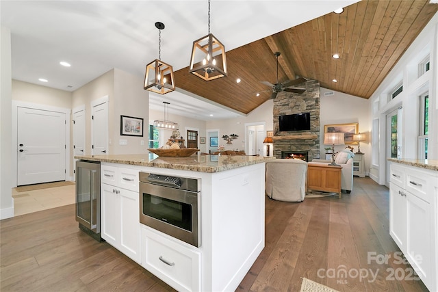 321 Middle Connestee Trl, Brevard, NC 28712 - kitchen with wine cooler, a fireplace, a ceiling fan, white cabinets, and light stone counters