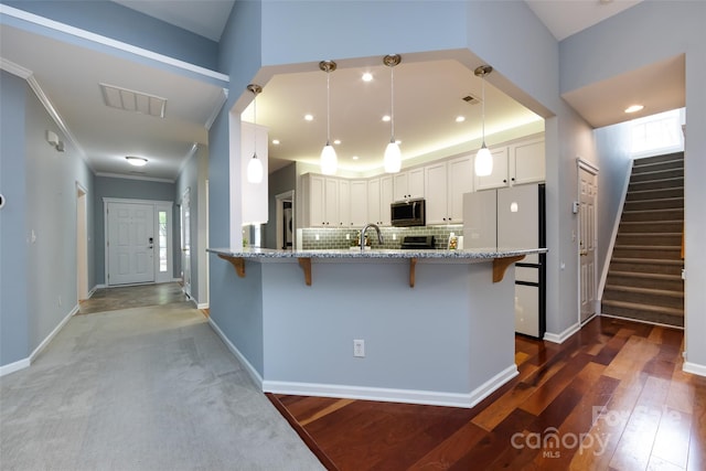 1040 Stonedown Ln, Matthews, NC 28104 - kitchen with a breakfast bar area, stainless steel microwave, freestanding refrigerator, a peninsula, and light stone countertops