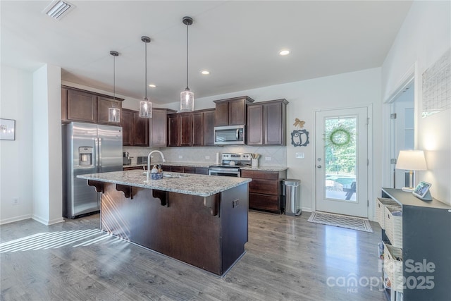 4113 Bent Green Ln, Monroe, NC 28112 - kitchen featuring appliances with stainless steel finishes, light wood finished floors, dark brown cabinetry, light stone counters, and a breakfast bar area