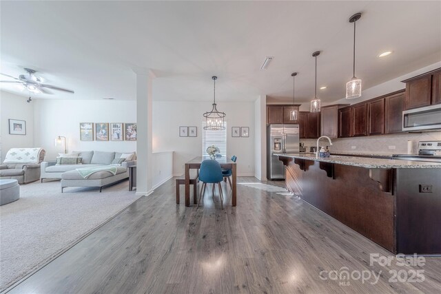 4113 Bent Green Ln, Monroe, NC 28112 - kitchen with stainless steel appliances, wood finished floors, a breakfast bar, light stone countertops, and dark brown cabinetry