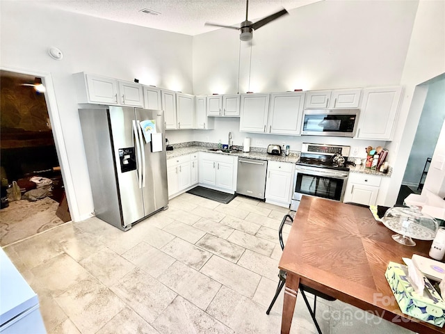 6007 Crosswood Ct, Charlotte, NC 28215 - kitchen featuring appliances with stainless steel finishes, high vaulted ceiling, a textured ceiling, light stone counters, and white cabinets