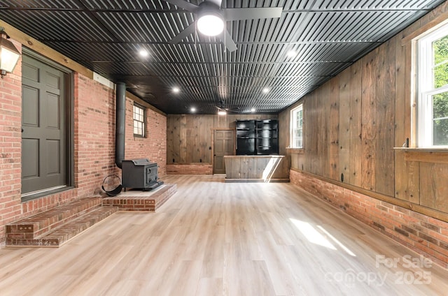 9410 Mountain Aire Cir, Charlotte, NC 28214 - unfurnished living room with a wood stove, brick wall, wood finished floors, wooden walls, and ceiling fan