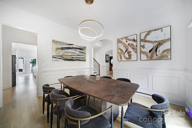 8016 Pemswood St, Charlotte, NC 28277 - dining room featuring arched walkways, light wood finished floors, crown molding, wainscoting, and a decorative wall