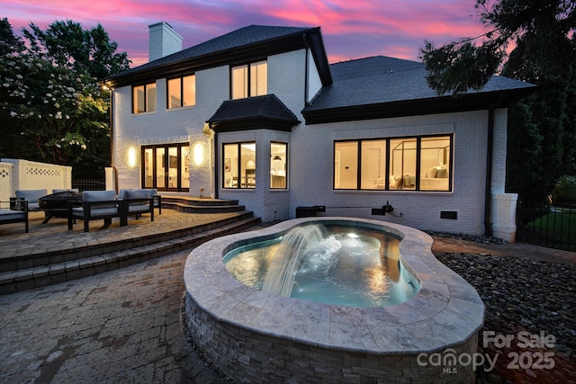 8016 Pemswood St, Charlotte, NC 28277 - back of property at dusk featuring brick siding, an outdoor hot tub, a chimney, a patio area, and an outdoor living space