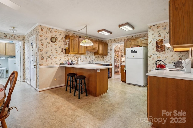 815 La Quinta Ln, Hope Mills, NC 28348 - kitchen with wallpapered walls, freestanding refrigerator, ornamental molding, a peninsula, and brown cabinets